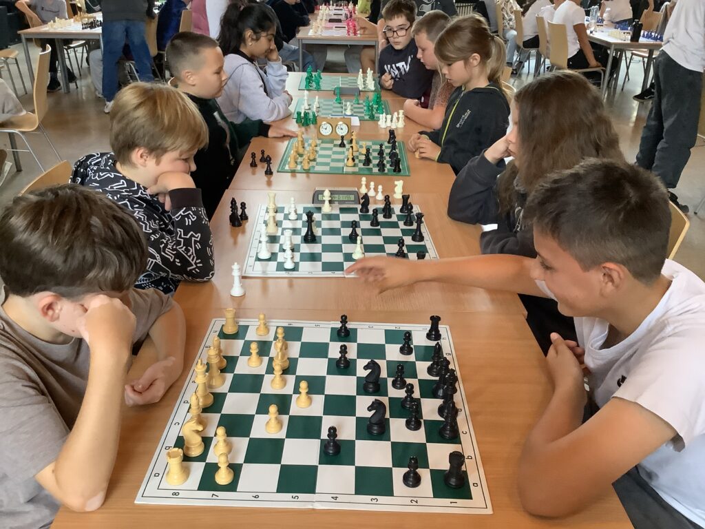 Kinder spielen bei einem Turnier paarweise Schach, sitzen sich an Tischen mit Schachbrettern gegenüber und konzentrieren sich auf ihr Spiel.