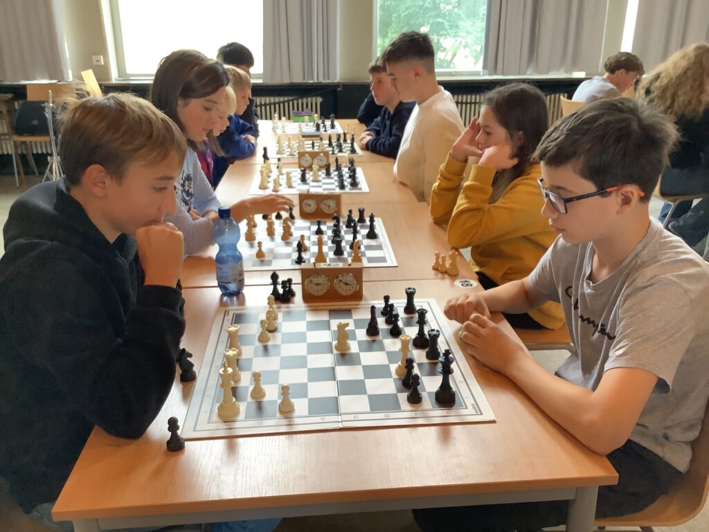 Eine Gruppe junger Menschen sitzt sich an Tischen gegenüber und spielt konzentriert Schach in einem Klassenzimmer.