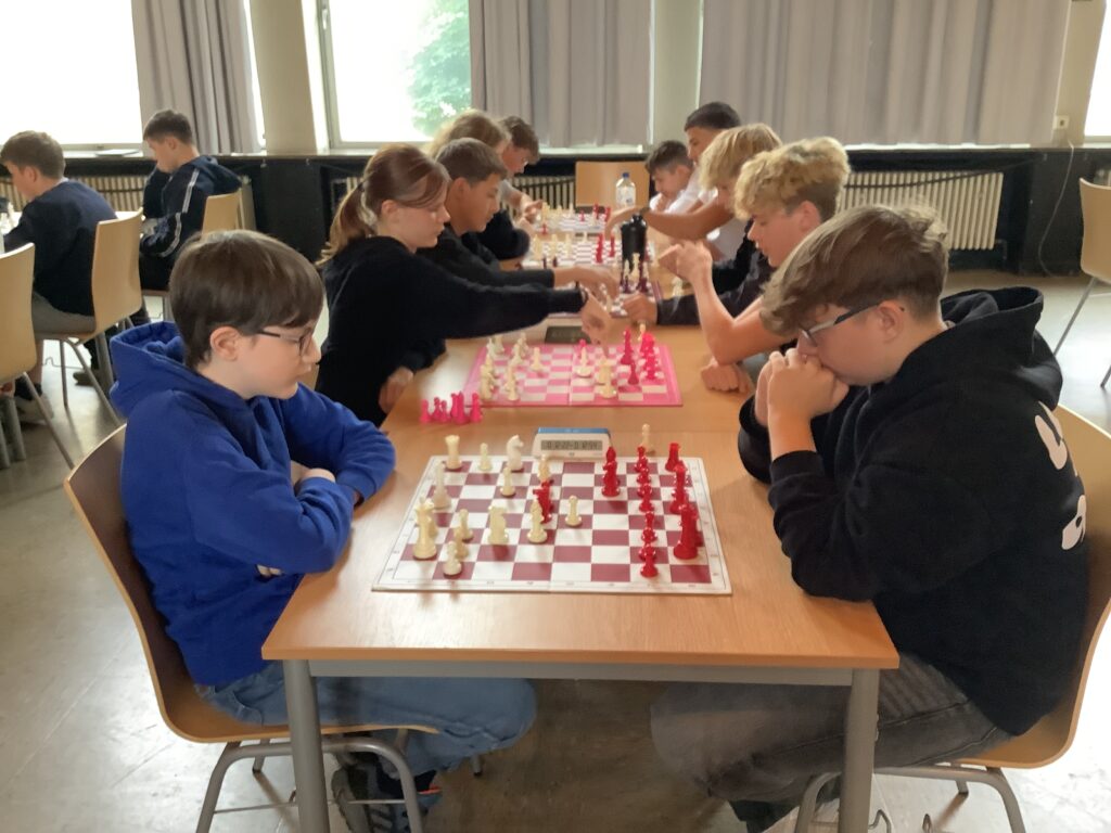 Die Kinder sitzen sich an Tischen gegenüber und spielen Schach in einem Klassenzimmer, konzentriert auf ihre Partien mit Schachbrettern vor ihnen.