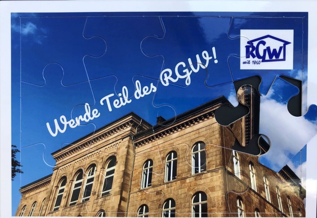 Ein Puzzlebild eines historischen Gebäudes unter blauem Himmel, mit dem deutschen Text Werde Teil des RGW! und dem RGW-Logo in der oberen rechten Ecke.