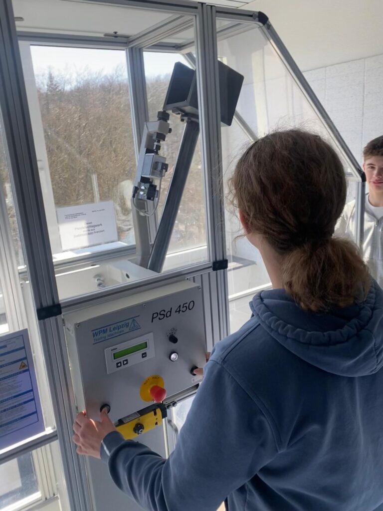 Eine Person bedient eine Psd 450-Maschine mit Tasten und einem Display, während eine andere Person in einem hellen Raum mit großen Fenstern daneben steht.