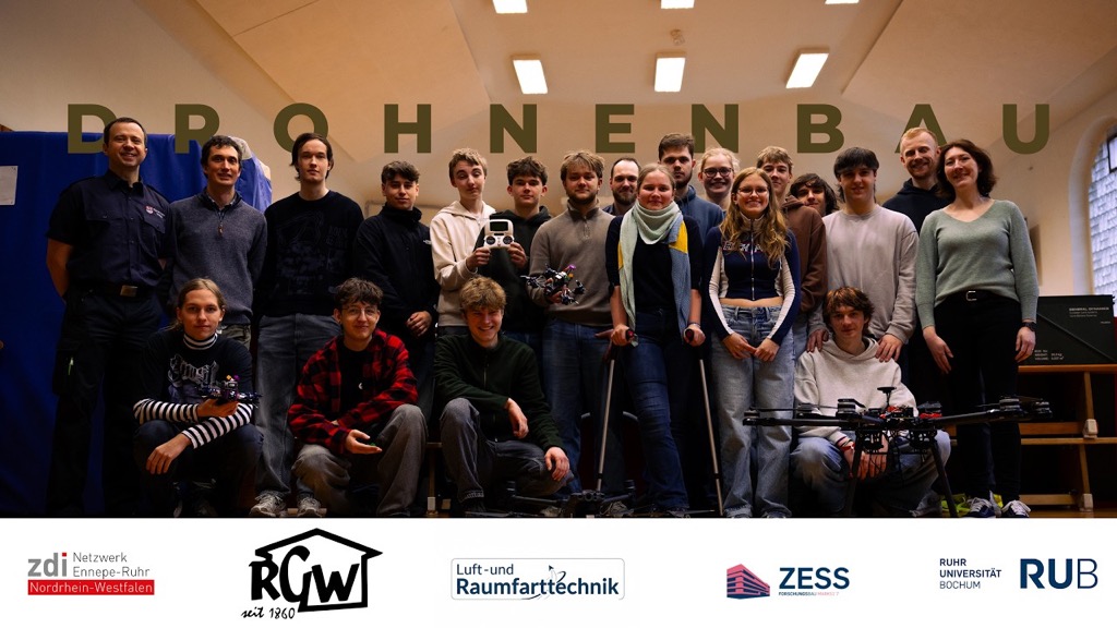 Eine Gruppe junger Erwachsener und zwei Erwachsene posieren in einem Haus mit Drohnen. Der Text lautet DROHNENBAU. Am unteren Rand sind mehrere Logos von Organisationen abgebildet.