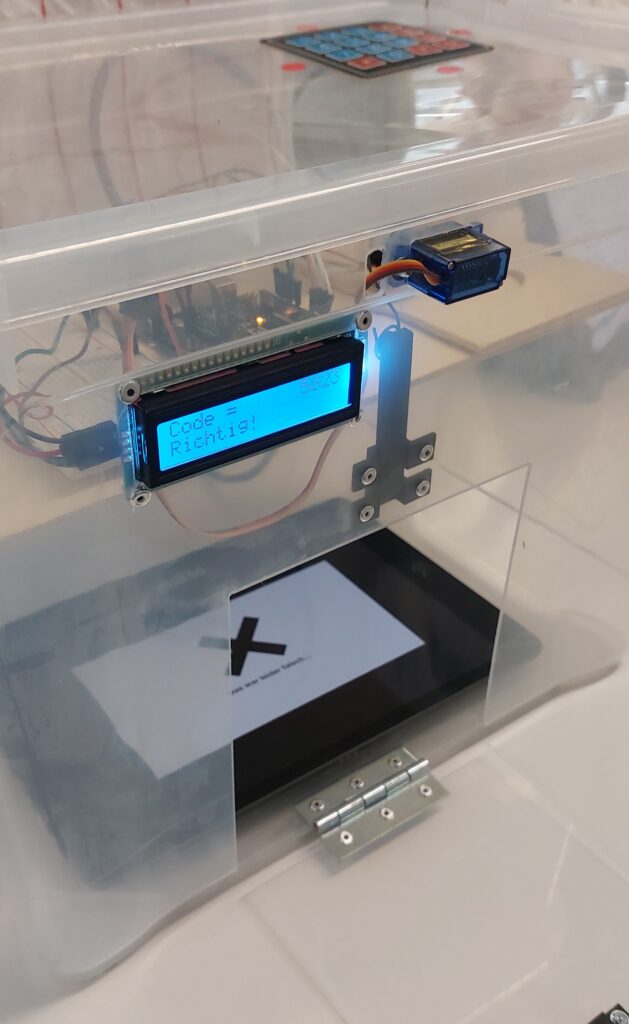 Auf einer durchsichtigen Schachtel mit einer elektronischen Anzeige steht über einem Servomechanismus und einem Zettel, auf dem ein großes X zu sehen ist, die Aufschrift „Code = Richtig!“.