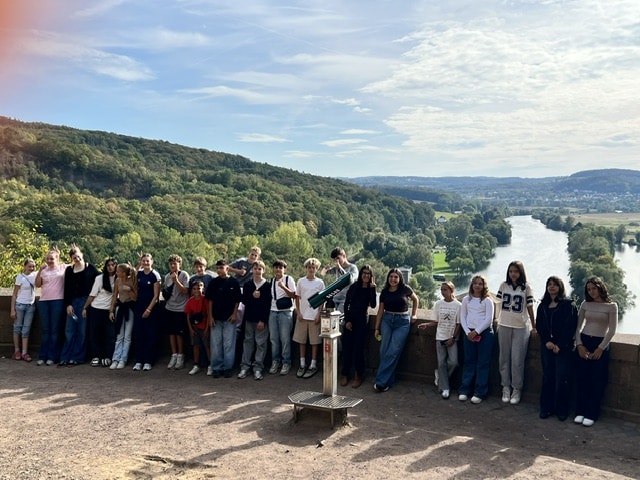 Eine Gruppe von Jugendlichen posiert für ein Foto auf einem Aussichtsfelsen über einem gewundenen Fluss und einem bewaldeten Tal.