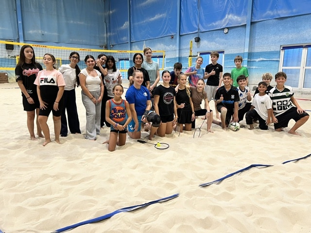 Eine große Gruppe von Jugendlichen, die auf einem Sandvolleyballfeld posiert.